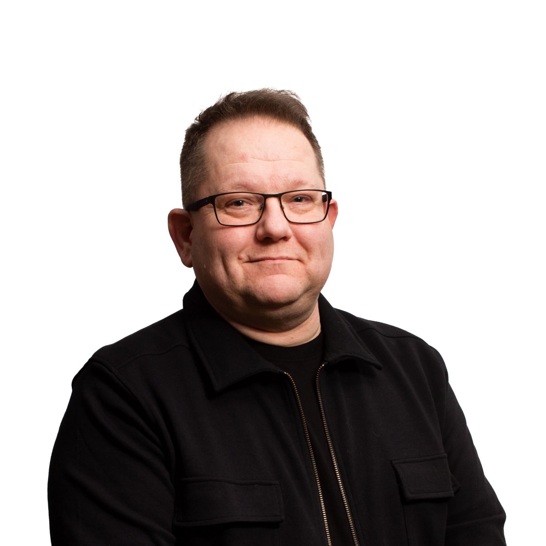 Keski-ikäinen, silmälasipäinen mies mustassa paidassa. Valkoinen tausta.