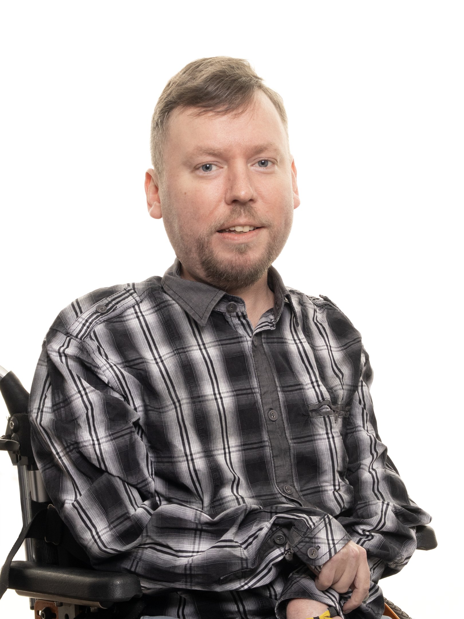 Ylävartalokuva pyörätuolissa sivuttain istuvasta ruskeahiuksisesta miehestä. Miehellä ruudullinen paita.