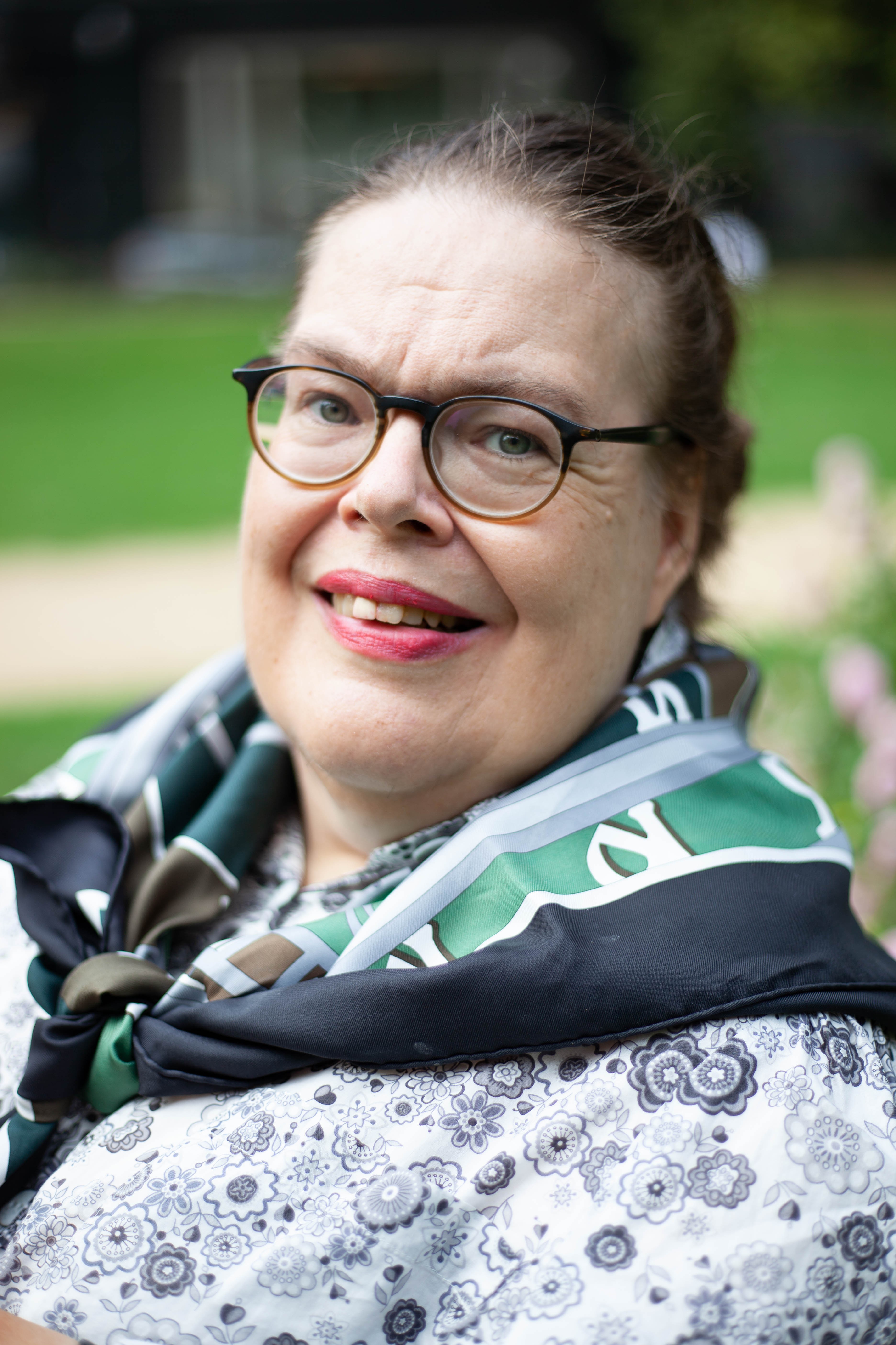 Kuvassa silmälasipäinen tummahiuksinen nainen katsoo hymyillen kameraan. Kuvassa on vain pää ja ylävartalo.